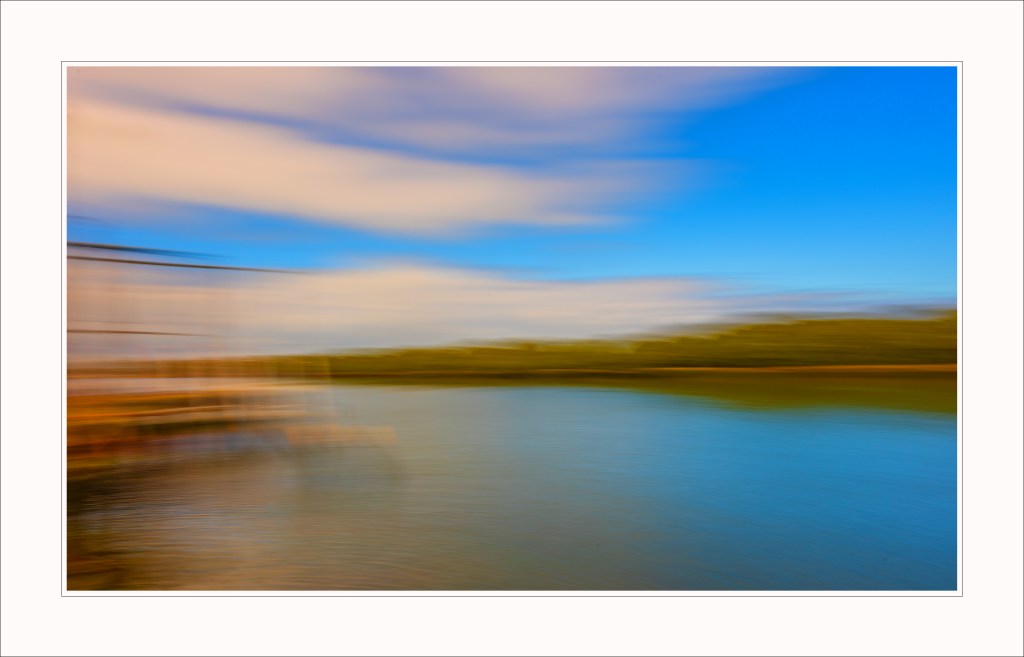 Abstract blurred landscape featuring a calm water body with soft, flowing clouds and greenery in the background.