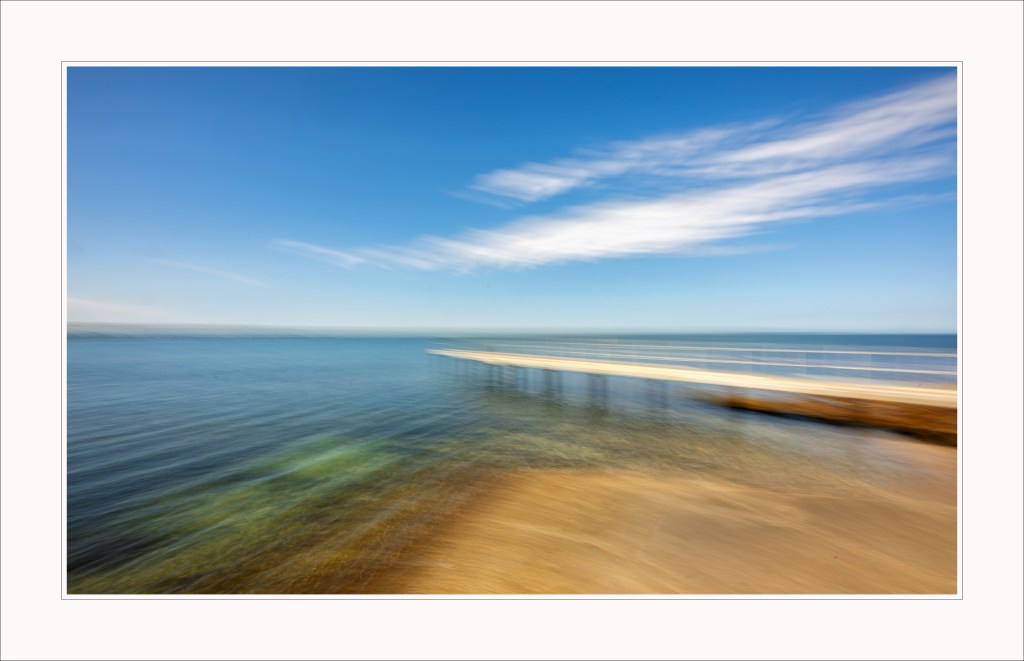 Serene view of a pier extending into calm waters under a blue sky with wispy clouds.